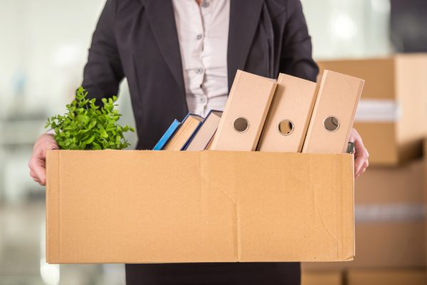 Persona sosteniendo una caja de cartón con carpetas libros y una planta dentro